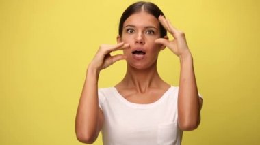 Güzel, sıradan bir kadın, sarı arka planda gevezelik edip duran iki eliyle taklit yapıyor.