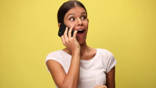 電話で話すカジュアルな女性は黄色の背景でニュースやお祝いの成功に驚いています — ストック動画