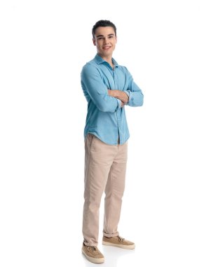 Uzun boylu, kendine güvenen, kot pantolonlu, kollarını kavuşturup beyaz arka planda dururken gülümseyen genç bir adam.