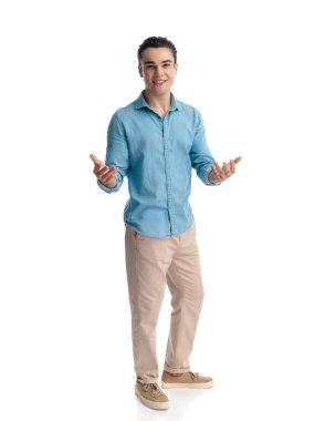 Beyaz arka planda ayakta durup gülümserken kollarını açıp davet eden kot pantolonlu çekici bir genç.