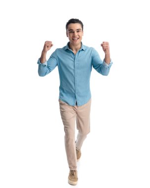 Mavi kotlu gömlekli heyecanlı sıradan bir adamın tüm vücudu havada ve zaferi beyaz arka planda yürürken kutluyor.