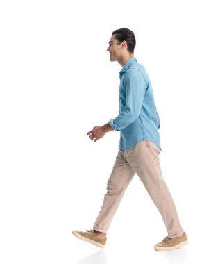 Beyaz arka planda yürüyen ve gülümseyen kot gömlekli mutlu sıradan bir adamın yan görüntüsü