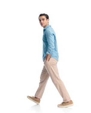 Mavi kotlu tişörtlü mutlu bir gencin yan görünüşü. Önüne bakıp beyaz arka planda gülümserken el ele yürüyor.