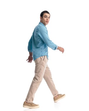 Mavi kot gömlekli, beyaz arka planda yürüyen ve ileriye bakan şaşırmış genç adamın yan görüntüsü.