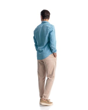 Arka planda mavi kot pantolonlu sıradan bir genç adam el ele tutuşuyor ve beyaz arka planda yürürken yan tarafa bakıyor.