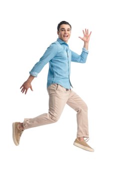 mavi kot gömlekli dinamik bir adam havada zıplıyor ve beyaz arka planda poz verirken heyecanlanıyor.