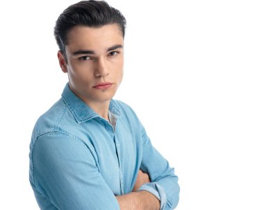 Mavi kot gömlekli çekici bir gencin yan görünüm portresi. Kollarını katlıyor ve beyaz arka planda ileriye bakıyor.