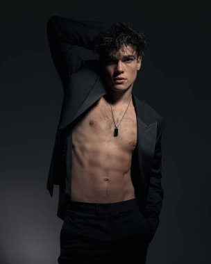 Siyah ceketli çıplak adam elini boynunun arkasına koyuyor ve cebinde havalı bir poz veriyor.