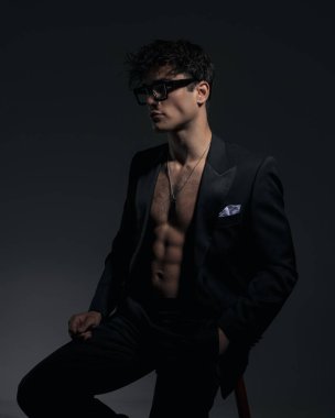 Siyah ceketli, gözlüklü, el ele tutuşan, yan yana oturan ve arka planda kaslarını gösteren şehvetli seksi bir adam.