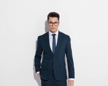 Lacivert takım elbiseli zarif genç işadamı. Gri arka planda dururken el ele poz veriyor.