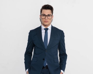 Lacivert takım elbiseli, el ele tutuşmuş ve gri arka planda duran genç, zarif bir adamın portresi.