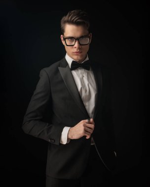 Çekici sağdıç portresi siyah smokin ayarlıyor ve siyah arka planda ileriye bakıyor.