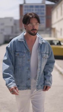 Romanya 'da yürürken ve etrafa bakarken mavi kot ceket düzenleyen gözlüklü sıradan moda adamı Sibiu