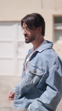 Mavi kot ceket ve gözlük takan, arkasını kollayan ve Romanya 'nın Sibiu kentinde dışarıda yürüyen genç adamın dikey videosu.