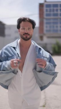 Gözlüklü, ceketli, gözlüklü seksi moda adamı göğsünü gösterip kendinden emin bir şekilde yakalı gömleğiyle dolaşıyor.