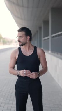 Gözlüklü, avuçlarını ovuşturan, ellerini cebine sokan ve kendinden emin bir şekilde dışarıda poz veren şık seksi bir adamın dikey videosu.