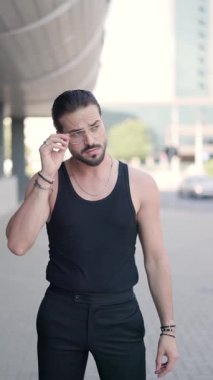 Siyahlar içindeki havalı moda adamı bardakları düzenliyor, el ele tutuşuyor ve kendinden emin bir şekilde dışarıda duruyor.