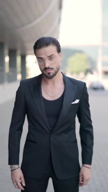 Yakışıklı genç adam avuçlarını ovuyor, yan yana bakıyor ve el ele tutuşuyor, gülümsüyor ve kendine güvenerek etrafına bakıyor ve ceketini tamir ediyor.