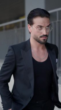 Siyah takım elbiseli, gözlüklü, elleri ceplerinde gezen, ceketini ve gözlüklerini tamir eden bir iş adamı.