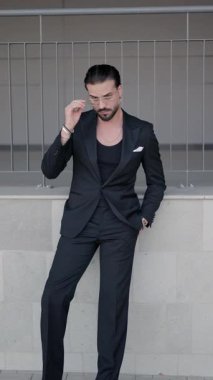 Siyah takım elbiseli zarif iş adamının el ele tutuşup yan yana baktığı, gözlükleri ayarladığı, siyah takım elbise açtığı dikey bir video.