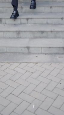 Siyah takım elbiseli şık bir iş adamı şehrin merdivenlerinde otururken güneş gözlüğü takıyor.