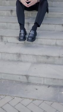 Dirsekleri dizlerinde oturan ve aşağı bakan genç iş adamının montunu ayarlarken çekilmiş dikey videosu.