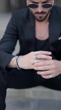 Siyah takım elbiseli şık bir adamın gümüş yüzüklerini gösteren bir video.