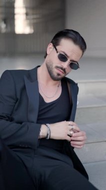 Güzel güneş gözlüğü takan çekici genç işadamı şehir merdivenlerinde yatarken gümüş yüzükler ve bilezikler takıyor.