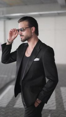 Havalı, zarif bir iş adamı, el ele hareket ediyor, güneş gözlüğü takıyor ve ceketini ilikliyor.