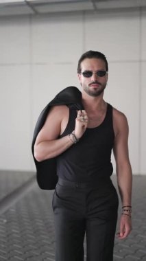 Güneş gözlüklü genç ve havalı bir işadamı ceketiyle omuz omuza yürüyor, güneş gözlüğü takıyor ve kendine güveniyor.