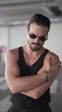 Çekici sakallı adam kollarını kavuşturup yan yana bakıyor, elleri ceplerinde hareket ediyor ve kendinden emin.