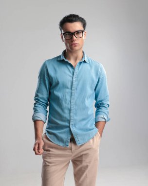 Mavi kot gömlekli seksi genç adam el ele tutuşup gri arka planda duruyor.