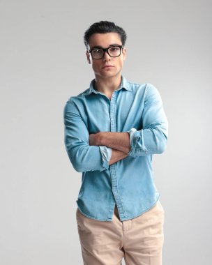 Kot gömlekli rahat bir adam kollarını kavuşturup gri arka planda duruyor.