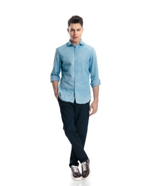 Beyaz arka planda elleri ceplerinde duran mavi kot gömlekli seksi sıradan bir adam.