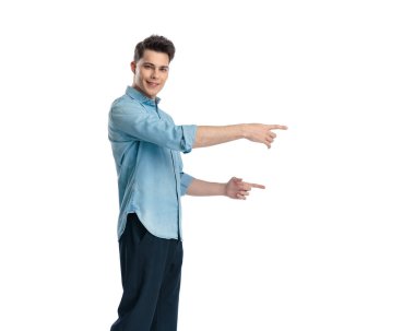 Kotlu tişörtlü mutlu bir adamın yan görünüşü. Parmakla işaret ediyor ve beyaz arka planda dururken gülümsüyor.