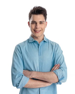 Mavi kot gömlekli kendine güvenen genç adam beyaz arka planda dururken kollarını kavuşturup gülümsüyor.