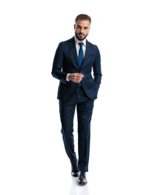 Lacivert takım elbiseli yakışıklı, beyaz arka planda elleri ceplerinde yürüyen zarif bir adam.