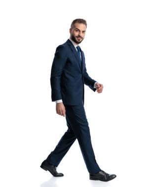 Lacivert takım elbiseli, beyaz arka planda yürüyen ve gülümseyen zarif bir adamın yan görüntüsü.