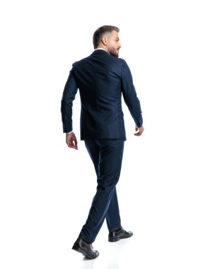Mavili lacivert takım elbiseli, beyaz arka planda yürüyen zarif olgun bir adamın arka plan görüntüsü.