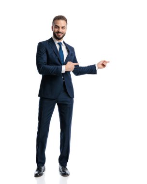 Lacivert takımlı yakışıklı genç adam beyaz arka planda dikilirken parmağıyla gülümsedi.