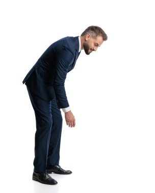 Lacivert takımlı zarif iş adamının beyaz arka planda öne eğilip gülümsemesinin yan görüntüsü.