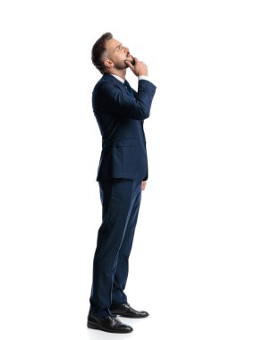 Lacivert takım elbiseli düşünceli bir işadamı. Çenesine dokunuyor, yukarı bakıyor ve beyaz arka planın önünde durup düşünüyor.