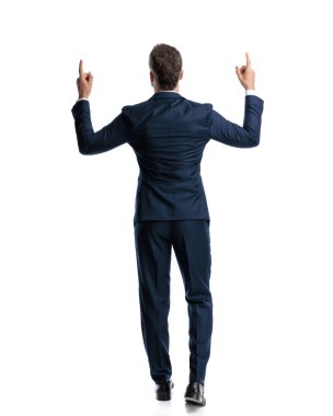 Lacivert takım elbiseli zarif bir adam gökyüzünü işaret ediyor ve beyaz arka planda yürüyor.