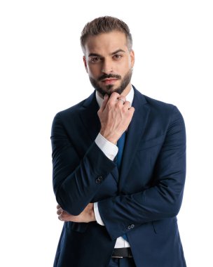 Lacivert takımlı, düşünceli, olgun bir işadamı beyaz arka planda dikilirken ileriye bakıyor ve merak ediyor.