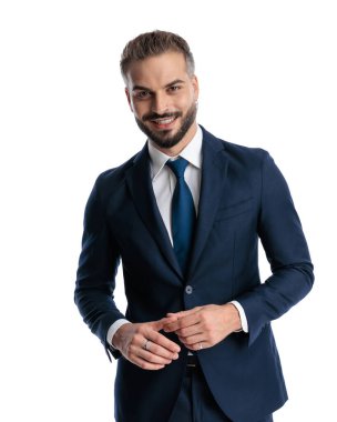 Lacivert takımlı mutlu olgun bir adam ileriye bakıyor ve gülümsüyor parmaklarına dokunuyor ve beyaz arka planda poz veriyor.