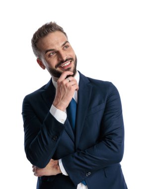 Deniz mavisi takımlı mutlu iş adamının portresi çeneye dokunuyor, yukarı bakıyor ve beyaz arkaplan önünde düşünüyor.