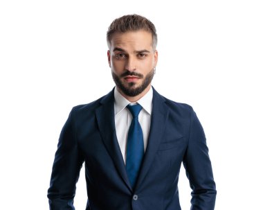 Şüpheli genç adam, lacivert takım elbise giyiyor. Beyaz arka planda dikilirken ileri bakıyor ve kaşlarını çatıyor.