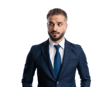 Meraklı, olgun, lacivert takım elbiseli bir işadamı beyaz bacakzemininin önünde dikilmeye çalışıyor.