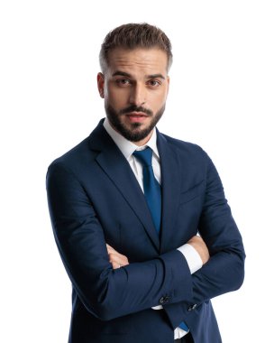 Lacivert takım elbiseli kendine güvenen bir iş adamı kollarını kavuşturup beyaz arka planda ileriye bakıyor.