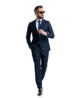 Lacivert takım elbiseli, güneş gözlüklü havalı olgun bir adam beyaz arka planda el ele yürüyordu.